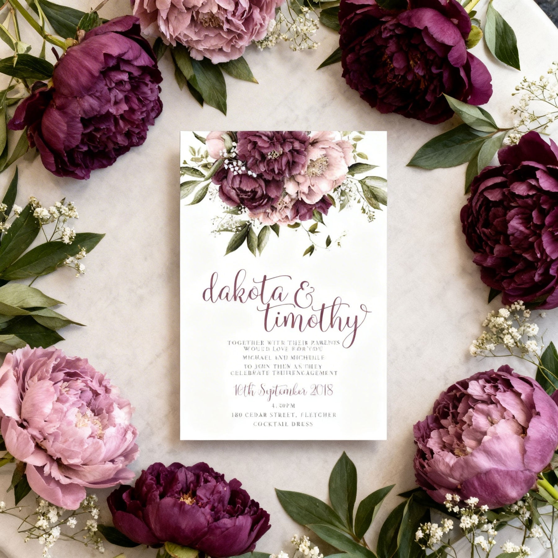 beautiful floral wedding invitation surrounded by burgundy and dusty pink peonie flowers