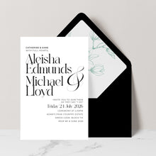 A wedding invitation card with elegant black typography on a white background, placed in front of a black envelope with sage green magnolia floral design.