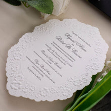 A white scalloped wedding invitation card with floral embossed detailing and black printed text in a beautiful shape