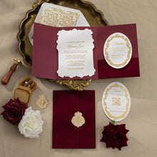 An elegant invitation suite laid out on a beige surface with a gold tray. The set includes a deep burgundy envelope, a matching envelope with a gold foil crest, a white lace-edged invitation card, a white reception card with gold detailing, a white registration card with a QR code and gold border, two burgundy roses, a white rose, and a small wooden wax seal.