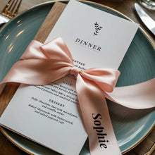 Wedding reception menu with a pink ribbon tied in a bow with guest name on a plate
