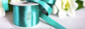 moonstone blue satin ribbon on spool on white table with white flowers