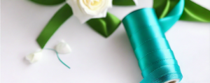 turquoise satin ribbon on spool on white table with white flowers