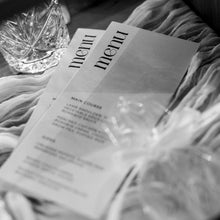 A black and white close-up of printed menus or cards laid on draped fabric beside a faceted glass object.