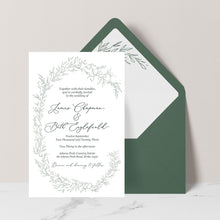 A wedding invitation card with a delicate green botanical wreath border and elegant script text, displayed in front of a dark green envelope on a light neutral background.