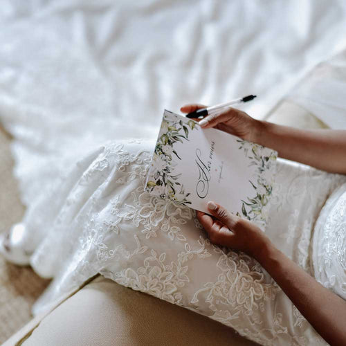 Bride holding a floral card and pen in a white bridal dress vow booklet custom design