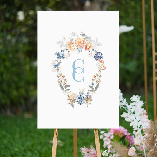 bridgerton inspired vintage floral wreath with monogram welcome sign blue and peach florals sitting on easel in garden 