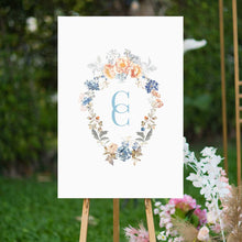 bridgerton inspired vintage floral wreath with monogram welcome sign blue and peach florals sitting on easel in garden 
