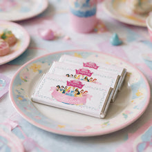 Three wrapped chocolate bars with Disney Princess labels are stacked on a pastel floral plate at a tea-time table setting.