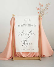 Wedding welcome sign with pink fabric and dried flowers on a stand.