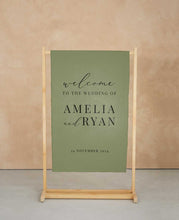 Green wedding welcome sign with wooden stand against a beige wall