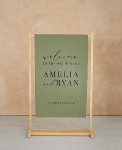 Green wedding welcome sign with wooden stand against a beige wall