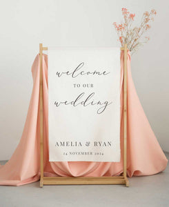 Wedding welcome sign with pink fabric and dried flowers on a stand.