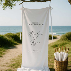 classic design welcome sign printed on white linen fabric and styled with ribbon hanging from a tree at a beach wedding ceremony