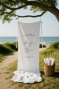 classic design welcome sign printed on white linen fabric and styled with ribbon hanging from a tree at a beach wedding ceremony