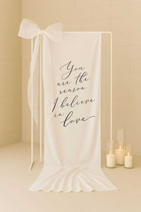 white linen fabric welding sign with saying you are the reason I believe in love styled with a large bow
