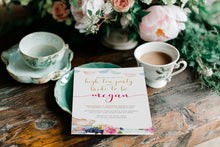 Teacup, saucer, and floral high tea bridal shower invitation on a wooden table with flowers in the background