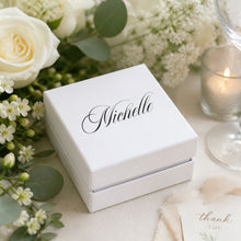 White marble tile coaster box with name decal, surrounded by flowers and a candle at a wedding reception, wedding favor