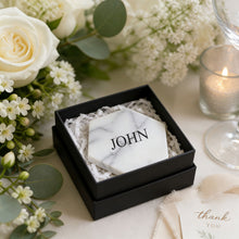 Marble tile coaster with name decal, inside a black box, surrounded by flowers and a candle at a wedding reception
