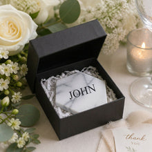 Marble tile coaster with name decal, inside a black box, surrounded by flowers and a candle at a wedding reception, wedding favor