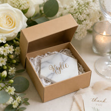 Marble tile coaster with name decal, inside a kraft box, surrounded by flowers and a candle at a wedding reception, wedding favor