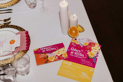 all-in-one colourful floral wedding invitation on a table with candles and fruit