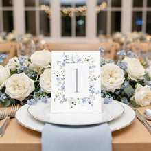 Decorative Primrose Spring table number card with floral design on a table setting with white roses and blue flowers.