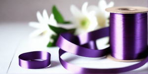 purple satin ribbon on spool on white table with white flowers