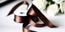chocolate brown satin ribbon on spool on white table with white flowers