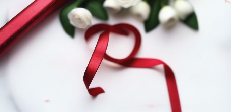 flame red satin ribbon on spool on white table with white flowers