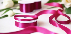 fuschia pink satin ribbon on spool on white table with white flowers