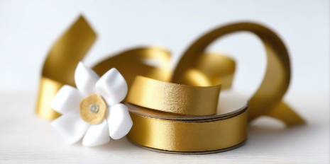 gold satin ribbon on spool on white table with white flowers