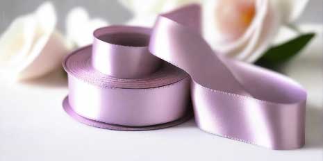 light orchid satin ribbon on spool on white table with white flowers