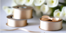 natural satin ribbon on spool on white table with white flowers