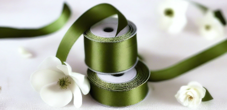 olive green satin ribbon on spool on white table with white flowers