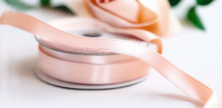 pastel peach satin ribbon on spool on white table with white flowers