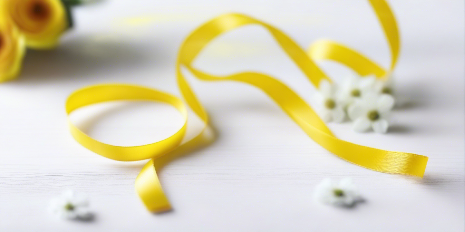 yellow satin ribbon on spool on white table with white flowers