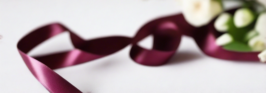 beetroot satin ribbon on spool on white table with white flowers