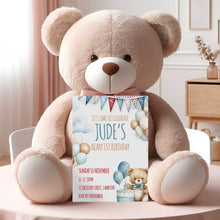 Large teddy bear holding a birthday invitation card on a table.