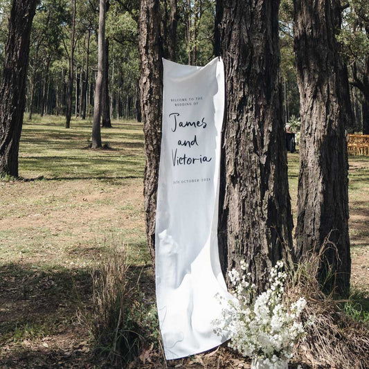 White wedding banner with text attached to a tree in a forest setting