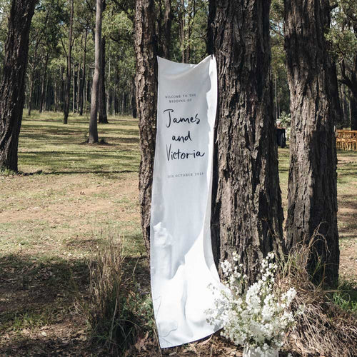 White wedding banner with text attached to a tree in a forest setting