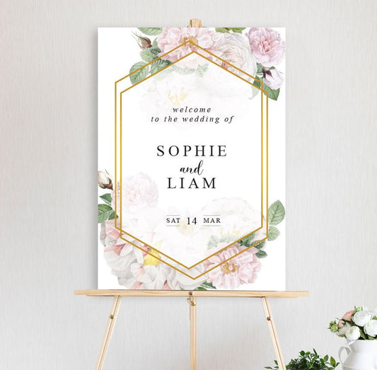 An welcome sign featuring a floral arrangement with peonies in white pink hues with gold border frame with a modern, classic font for engagement, wedding, birthday