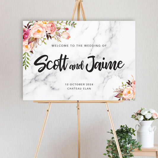 An welcome sign featuring a floral arrangement with peonies in pink and peach hues with marble background with a script font for engagement, wedding, birthday