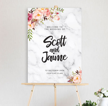 An welcome sign featuring a floral arrangement with peonies in pink and peach hues with marble background with a script font for engagement, wedding, birthday