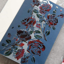 Floral rose laser-cut wedding invitation featuring roses on the panels, shown in navy with design showing through