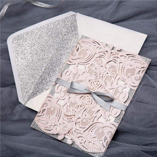 Blush pink laser-cut wedding invitation featuring silver ribbon, white envelope and silver glitter envelope liner