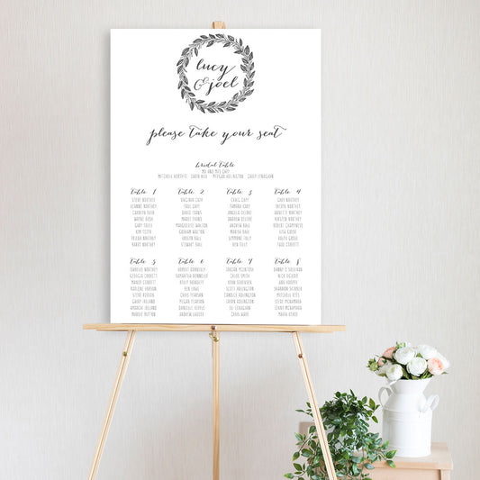 black and white wreath design table seating chart sitting on a timber easel