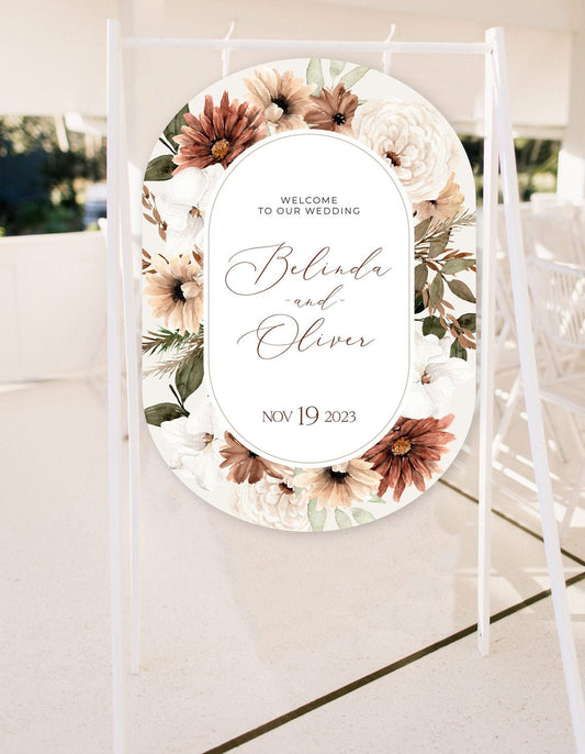 a bohemian floral welcome sign featuring peonies and daisy in autumn brown and neutral tones, diecut to double arch shape and hanging from a sign rack
