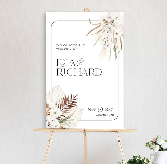 white orchid bouquet with dried pampas grass and palm leaves with a black border border welcome sign